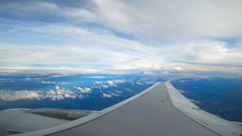 An airplane wing above bright white clouds under a blue sky